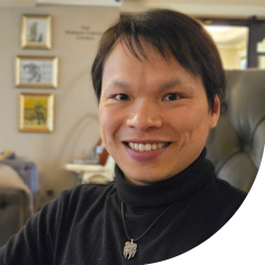 A man with short dark hair wearing a dark turtle neck top smiling at the camera.