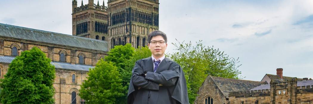 Dr Yang Li stands on Palace Green, Durham ahead of congregation with Durham Cathedral visable in the background behind him.