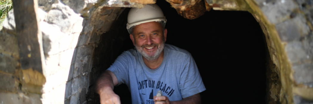 Professor Chris Gerrard, wearing a protective hard hat, at the top of a ladder at an archaeological site, smiling to camera