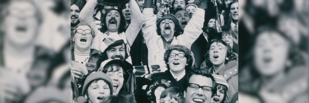 Black and white picture of male and female football fans cheering.