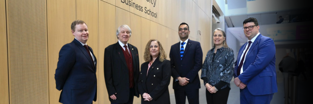 A mixed group of smartly dressed men and women standing in a line smiling at the camera inside Durham University Business School