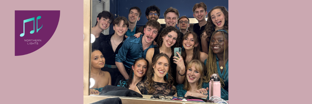 A mixed group of students squeezed together taking a selfie in a backstage mirror.