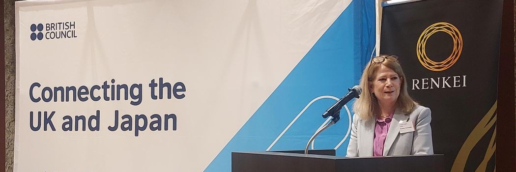 A speaker standing at a podium in front of UK-Japan and RENKEI banners
