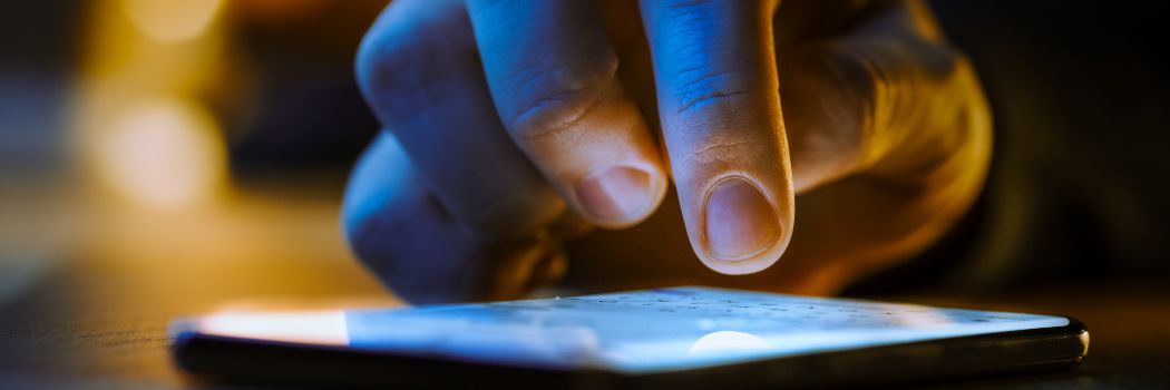 A close up of a man's hand over the lit up screen of a mobile phone.