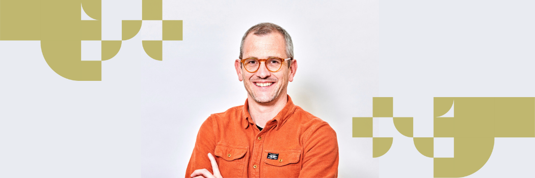 James Rowlands wearing an orange top smiling with his arms folded