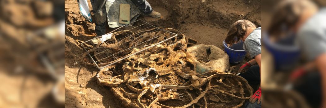 Archaeologists carefully excavate tangled metal from a trench in a field