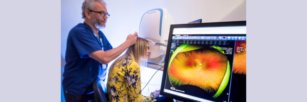 A male doctor adjusts a headset worn by a woman sitting in front of a computer screen