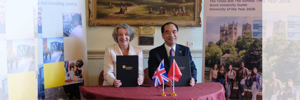 Professor Karen O'Brien and President Gong sitting at a table smiling with UK and China flags