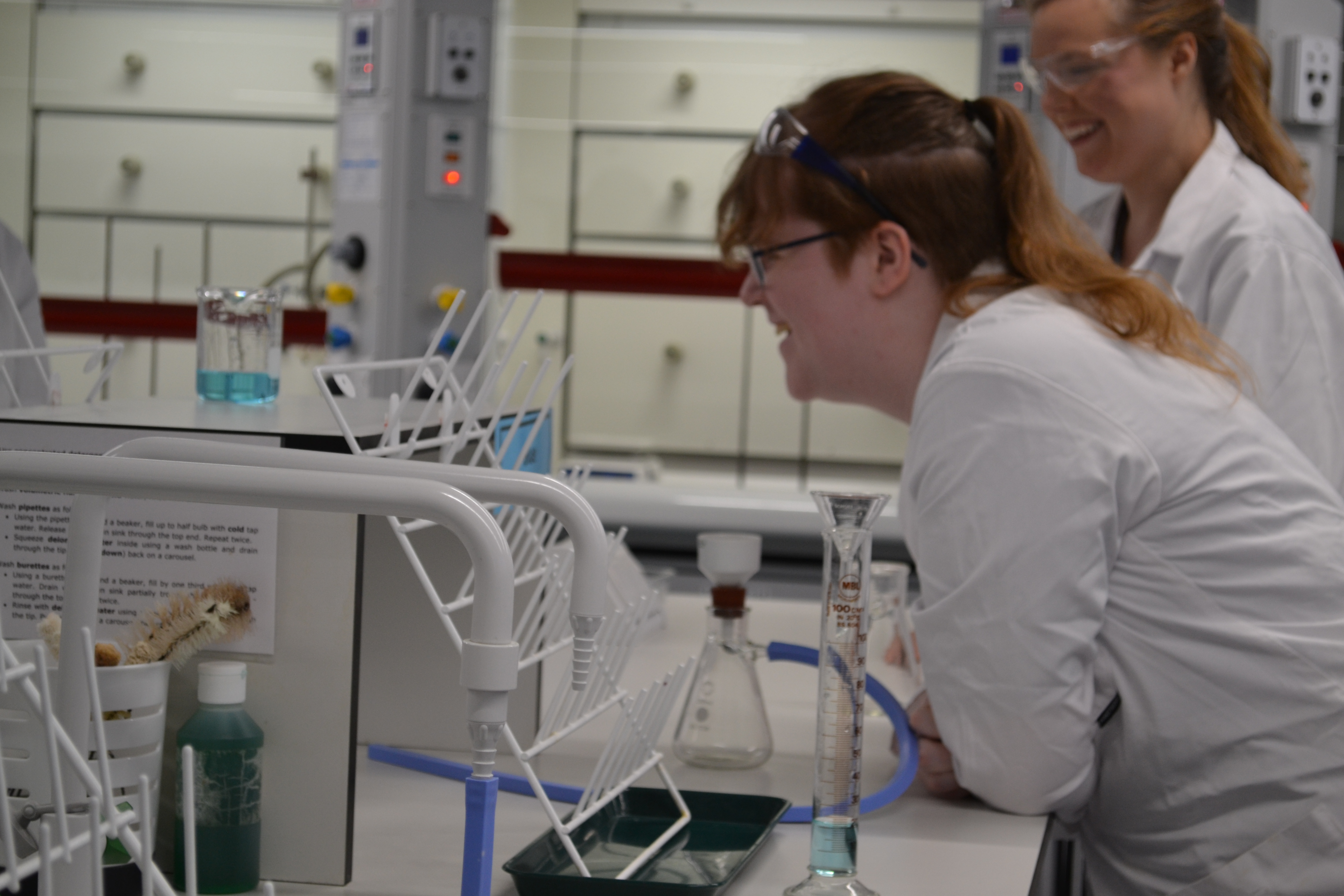 Two students smile as they undertake an experiment at a lab bench.