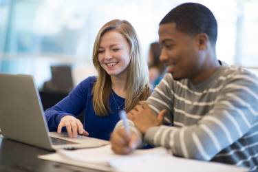 Two students sitting side by side working on a laptop
