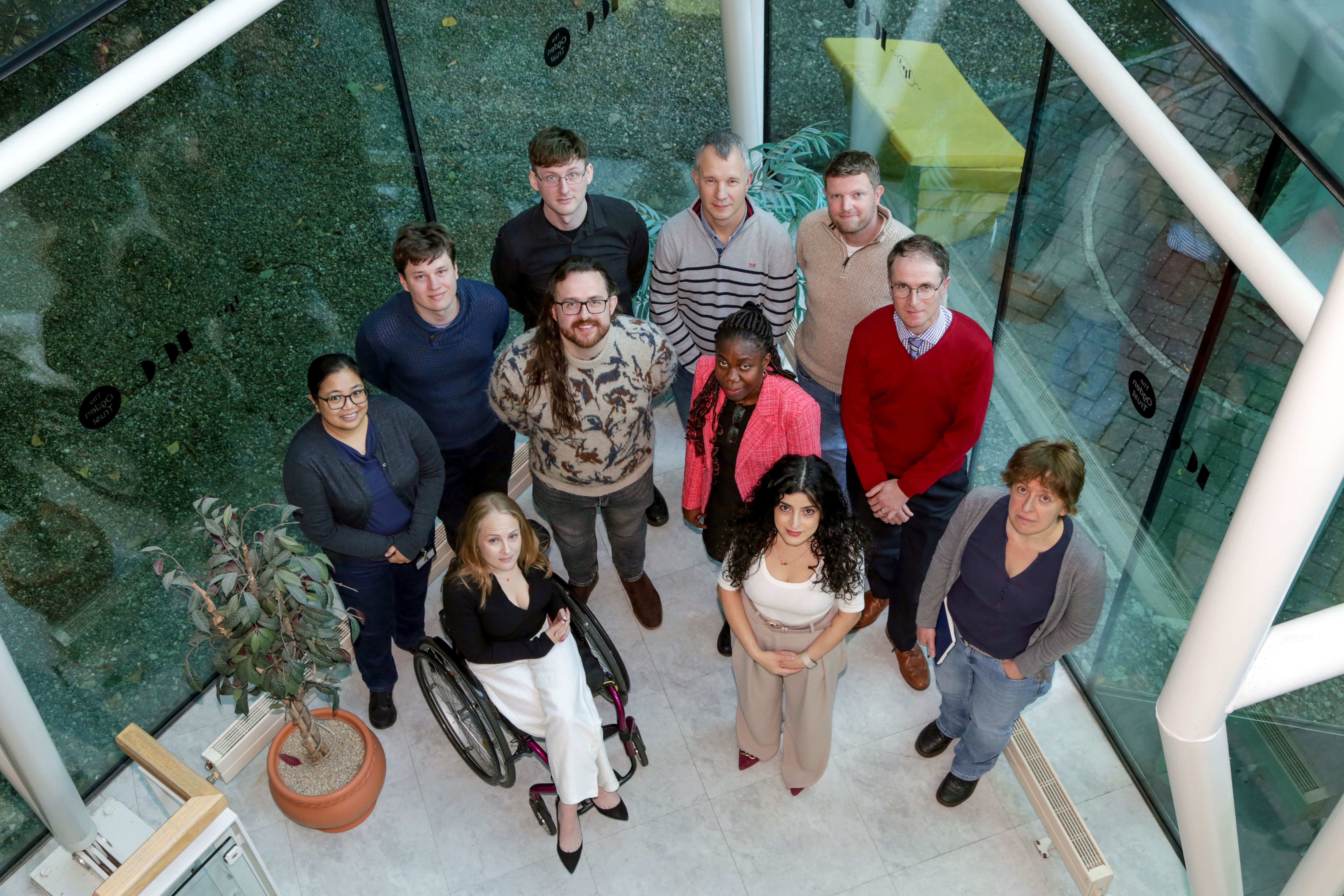 Members of the PhES group photographed from above looking up at camera, pictured in the glass walled lobby of the Ogden Centre