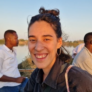Woman with black hair smiles widely at camera with two men in the background