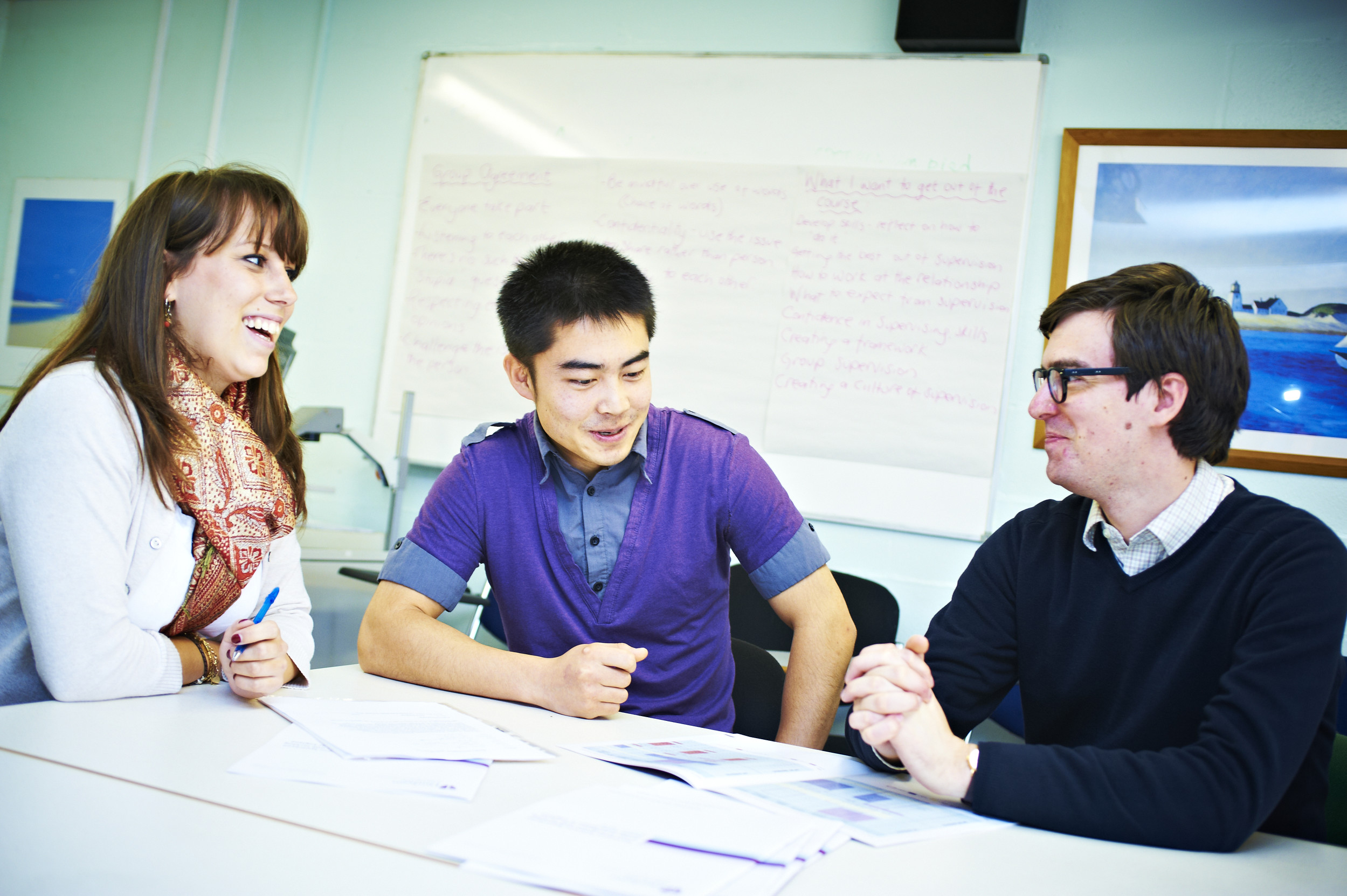 Students sat round a table laughing with their tutor