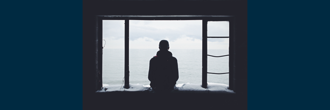 A silhouette of a person looking out of a bright window