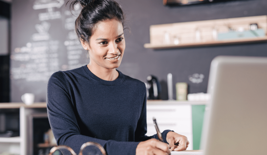 A woman looking at a laptop with pad and pen
