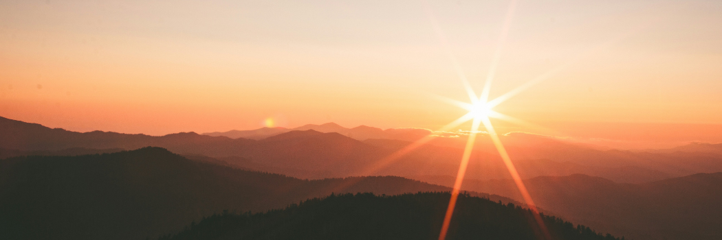A sun rising over mountainous terrain.