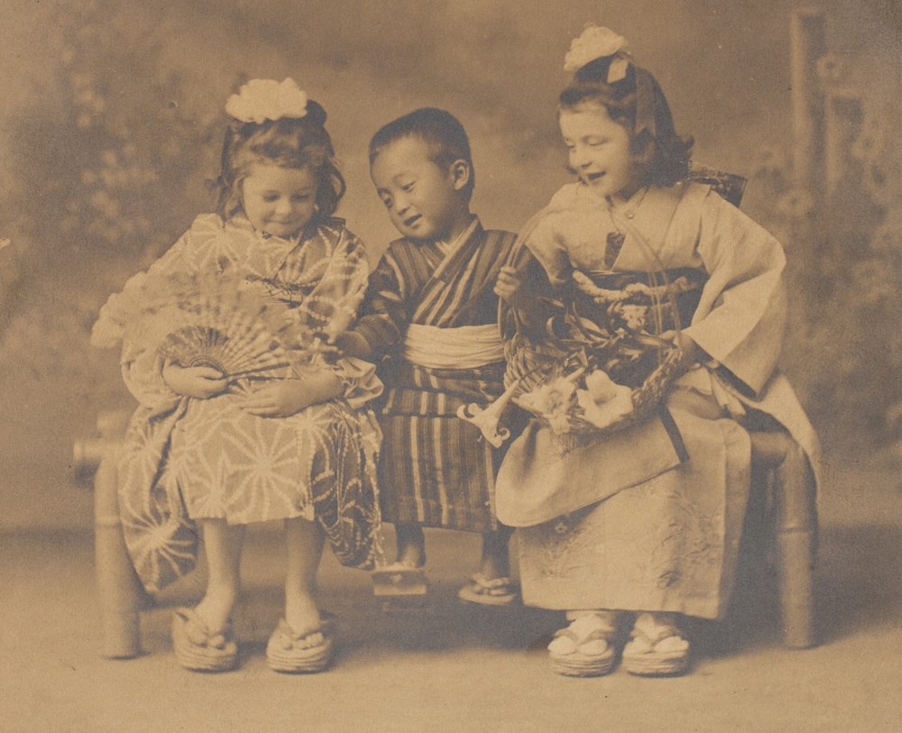 Two European girls sit either side of a Japanese boy on a bench