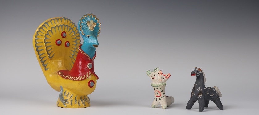 Group of three toys, one is a large yellow and blue rooster, and the smaller two are a black horse and a white fantasy creature with two heads.